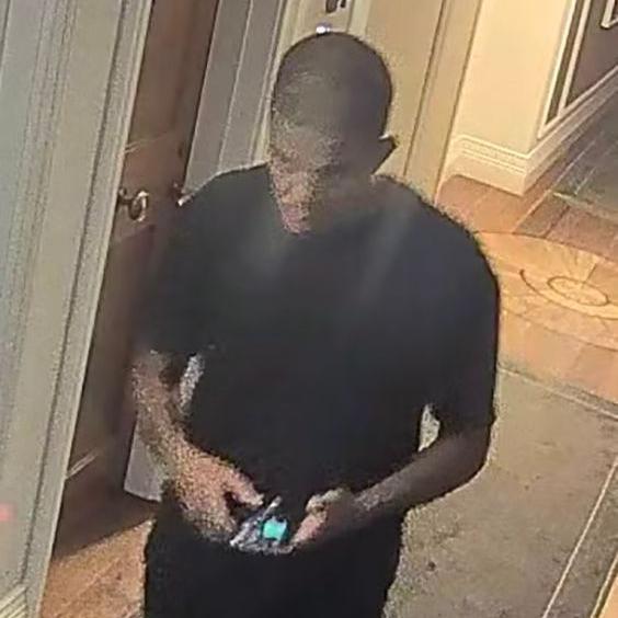 Still from grainy CCTV footage showing Mussie Imnetu walking while looking at a lit-up phone screen. He is dressed in black trousers and a black T-shirt. It is after dark and the lighting is from an orange street light.