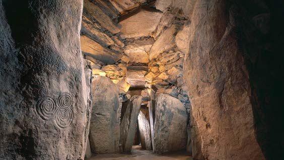 Inside a stone cave, swirls can be seen to the left of the picture which have been carved into the rocks.