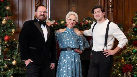 The judges: A man wearing a black velvet suit and bow tie, a woman wearing a blue star print dress and a man in a white shirt with black trousers and suspenders. 