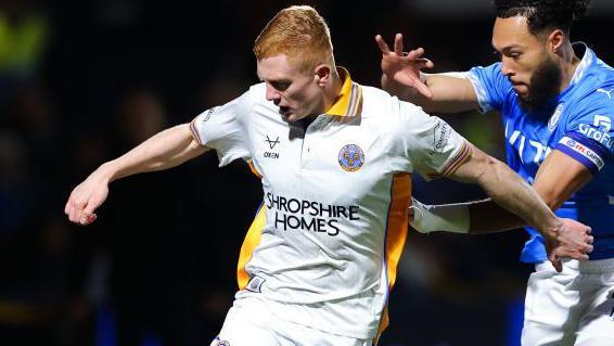 Shrewsbury defender Morgan Feeney is challenged by Stockport's Kyle Wootton at Edgeley Park