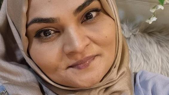 A selfie of a woman sitting against a fluffy white pillow and wearing a hijab. 