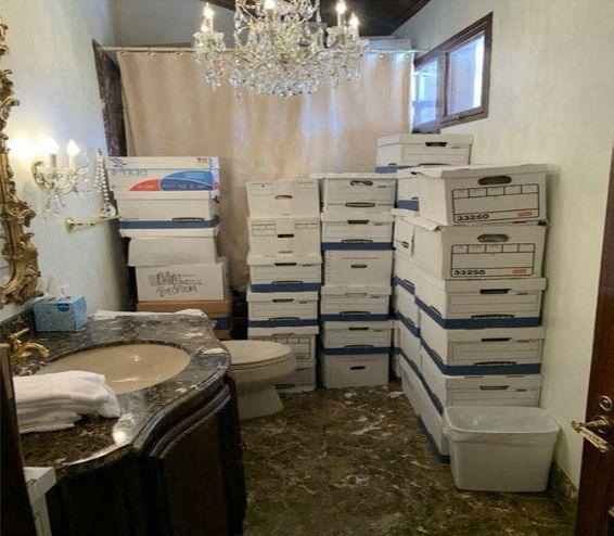 Dozens of white boxes are piled up in a bathroom with a sink, toilet, shower and ornate fittings including a chandelier 