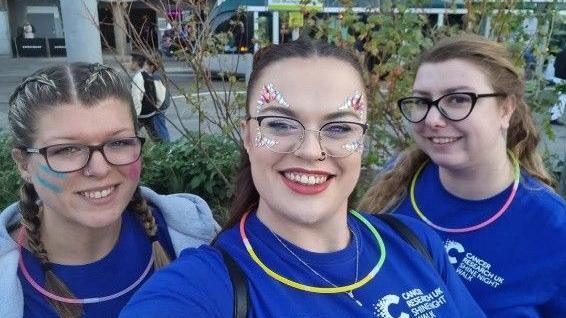Lauren Moger, with two friends, in Nottingham's Market Square, wearing fundraising t shirts and holding glow sticks