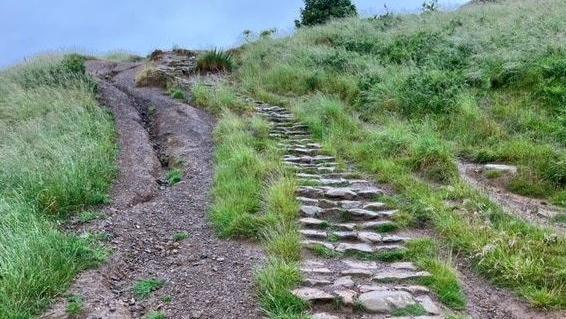 Pathway leading up to Roseberry Topping. The stones on the left are well worn and there is a gully running parallel to the path.