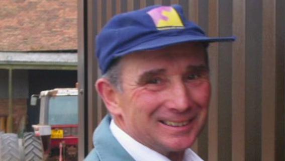 Rocky Poulson stood in front of a tractor wearing a blue hat 