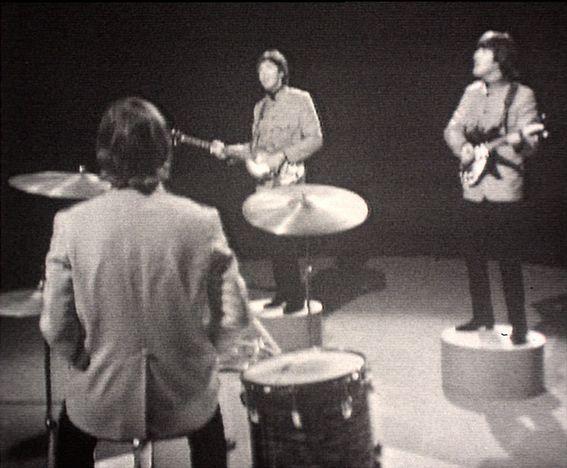 Screenshot of the back of Ringo Starr playing the drums, with Paul McCartney and John Lennon on podiums playing guitars and singing