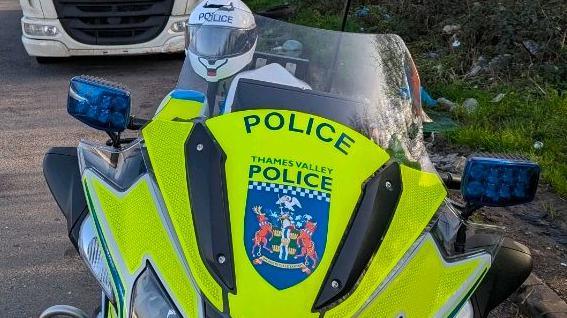 A police motorcycle is parked on the side of a road with part of a lorry visible in the background.