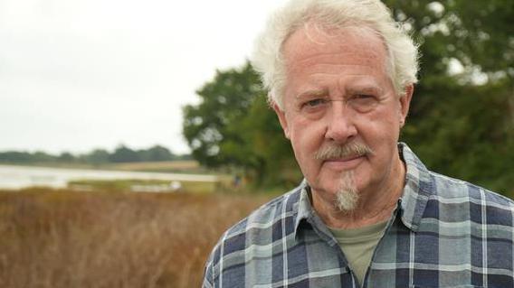 Peter Clitheroe standing by the shoreline on the River Alde at Iken in Suffolk