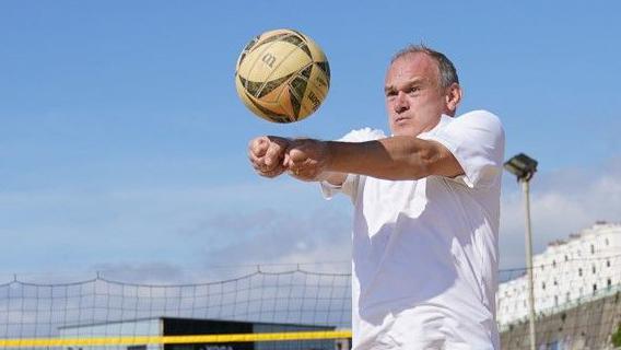 Liberal Democrat leader Sir Ed Davey plays volleyball on a visit to Brighton Beach on Sunday. Davey can be seen concentrating on hitting the ball next to a volleyball net.