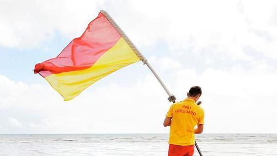 A lifeguard holding a red and yellow flag near the sea