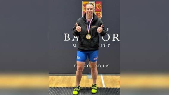 A woman with a gold medal and her thumbs up.