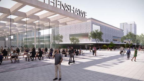 Artists impression of new shopping centre which shows a large glass building with the word Wythenshawe in large letters on the canopy roof. People are sitting on picnic benches in a pedestrianised courtyard. In the background there is another grey building with the words Culture Hub written across it