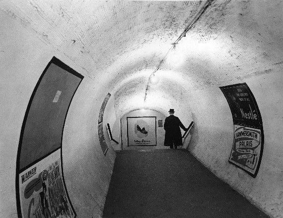 Passageway at Tottenham Court Road Underground station shows man in top hat and posters for Hammersmith Palais, by Topical Press, 1946