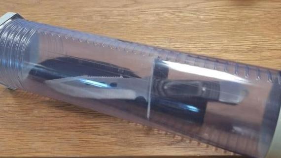 A hunting knife is placed into a plastic container, which is on a wooden table.
