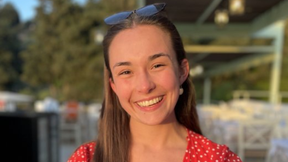 A smiling woman with brown hair wearing a red spotted top and with sunglasses on her head.