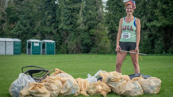 Gill Thomas is standing on a lawn with rubbish bags in front of her. She is wearing a running outfit and is smiling at the camera.