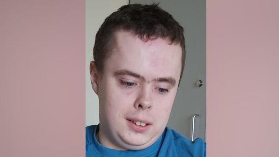 A man with dark hair looking downwards. 
he is wearing a blue t-shirt