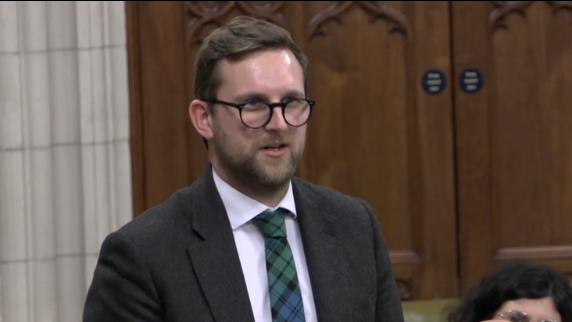 Henley MP Freddie van Mierlo speaking at a Westminster Hall debate - he is wearing a dark grey suit and checked green and blue tie. 