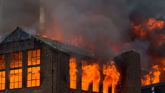 Image shows the windows of the Hotspur mill with flames leaping out of them.
