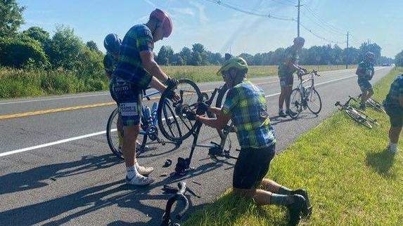 Two cyclists on the road bent over fixing a bike