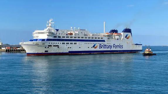 A white ferry with blue tipped chimneys with the words Brittany Ferries on the side arriving in St Peter Port Harbour.