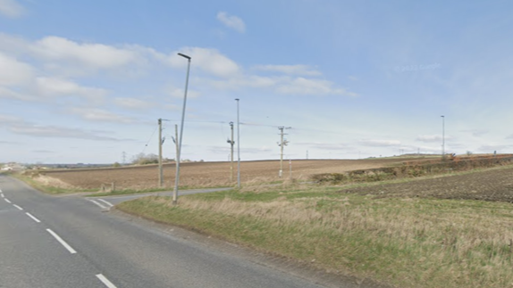 Countryside road with fields and a cloudy blue sky