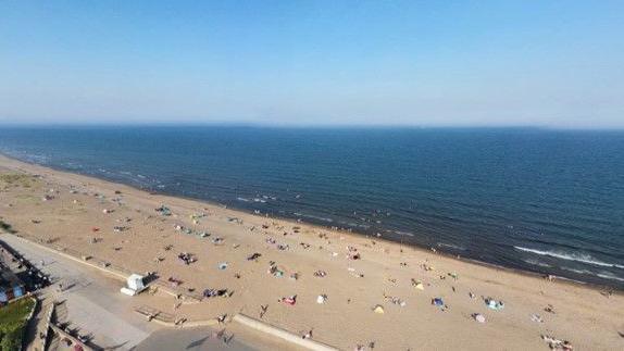 Sandy beach with people sitting on it. There is a blue sea and blue sky.
