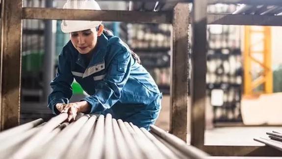 Woman with white hard hat on lifting a grey pipe