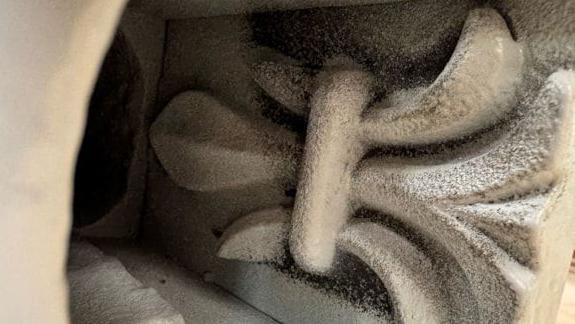 A piece of grey ironwork with an engraving on it in a rectangular shape. You can see a wooden wall and floor behind it.