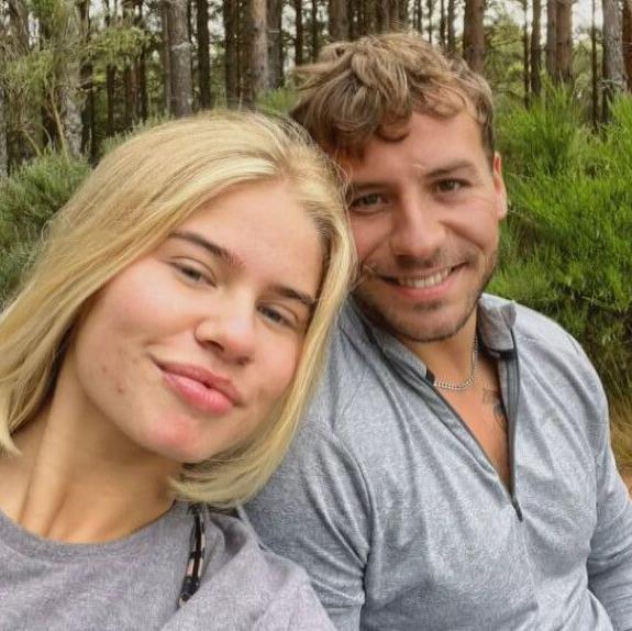 A woman with blonde hair and a man with brown pose for a smiling selfie in a forest