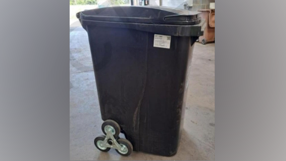 A black wheelie bin which has been modified with three wheels on each side.
