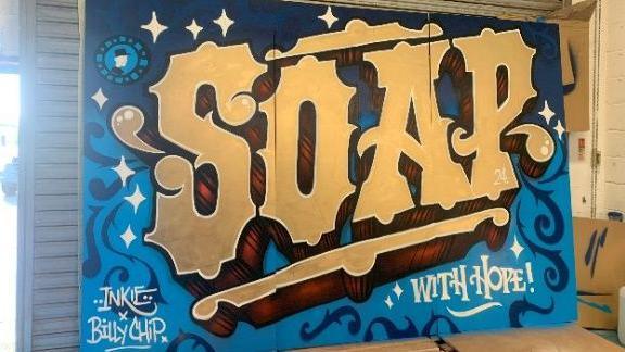 The mural by Inkie at the Somerset Toiletry Company. The mural reads 'Soap' and is gold and blue in colour.