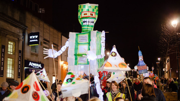 A nighttime shot of a robot-style lantern towering above a parade of people, many holding smaller lanterns on long sticks, on a street in Bedminster.