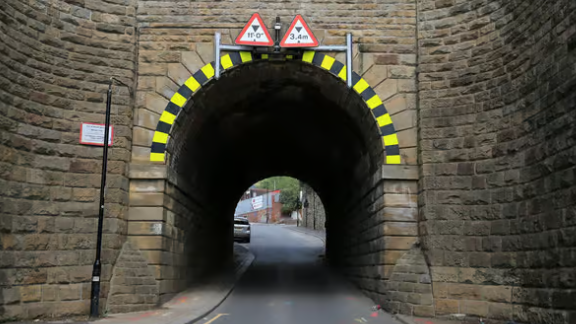 A narrow dark tunnel on a road surrounded by stonework. A car is parked up at the far side of the tunnel