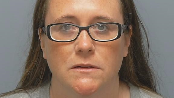 Alice Mackey custody image from police. She is a woman with loose brown hair and black-rimmed glasses looking directly at the camera.