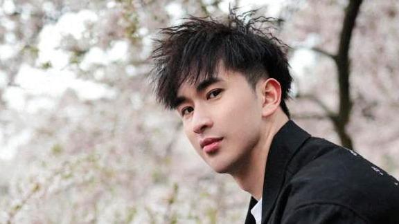 Zou is looking towards the camera with cherry blossoms in the background
