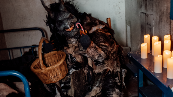 A person is dressed up as a witch in an old prison cell. There are lit candles next to the person.