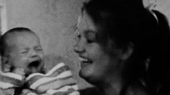 A black and white photo of a woman smiling whilst holding a crying baby.