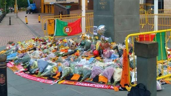Floral tributes have been left at Molineux Stadium in Wolverhampton. There are yellow barriers surrounding the tribute and scarfs and flags adorning the display.