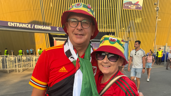 A woman and a man look at the camera. They both have red Welsh shirts on and bucket hats in the Welsh colours of red, green and yellow.