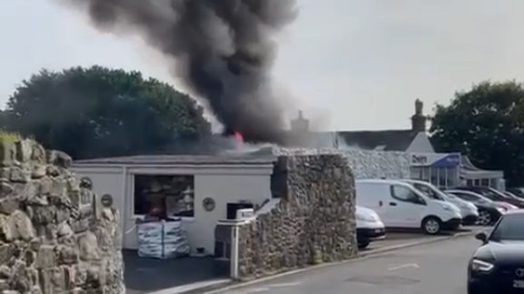 A plume of smoke and some flames rise above a garage