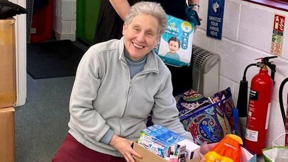 Jenny kneeling on the floor packing Christmas parcels at a charity