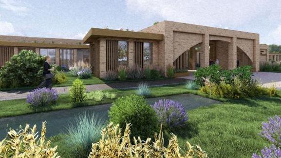 Single-storey brick crematorium featuring arched entrance area, with lawn and ferns in the foreground.