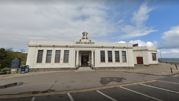 White building with 'Beach Ballroom' wording in block capitals, under a cloudy blue sky, and sea in distance.