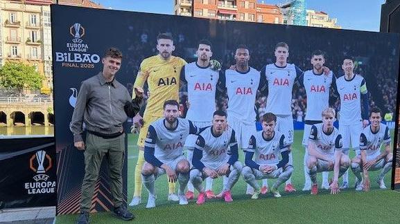 Alfie Watts, who won BBC's Race Across the World last year, in front of a Tottenham team photo