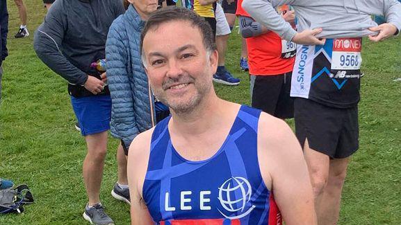 Lee Rawlinson smiling at the camera in running attire  
He has just or is about to compete in a run. 