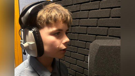 Aaron wearing headphones and standing in front of a microphone while he is recording his new song.