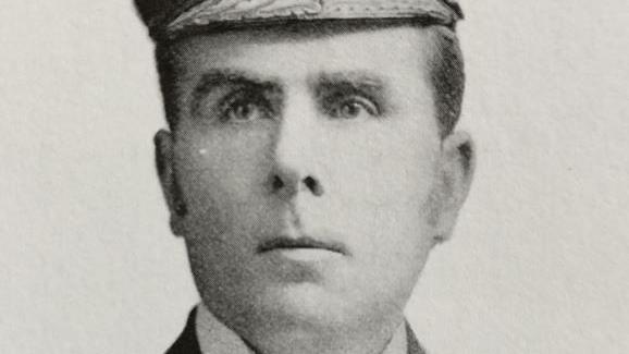 A black and white close up of a man with dark hair and a cap.