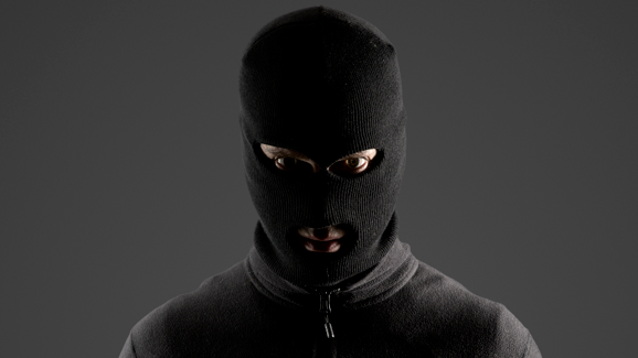 A person wearing a black balaclava and a black jumper, looking directly at the camera. 