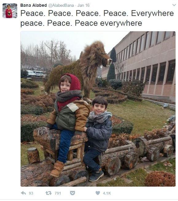 A screenshot from the Twitter account @AlabedBana, showing her two younger brothers smiling and seated on a a row of plant pots made in the shapes of a train. The caption reads "peace everywhere".